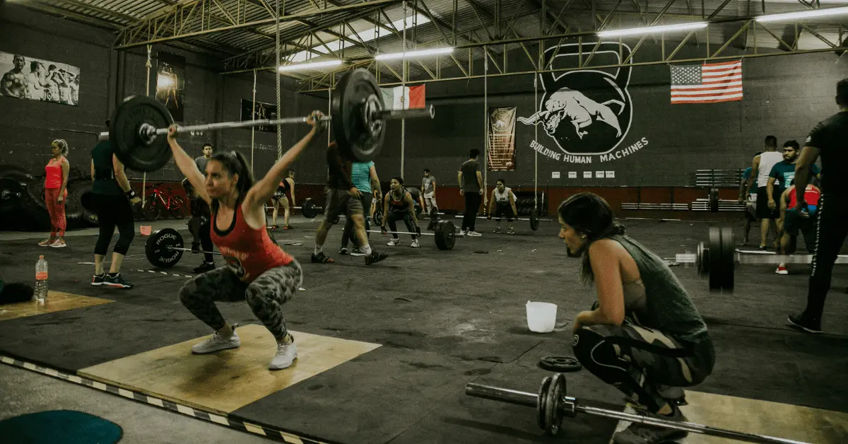Powerlifting Classes in Dallas: How to Train for Real Strength Without Going It Alone Athletes participate in a group weightlifting class, practicing Olympic lifts and strength training under coach supervision in a busy gym environment.