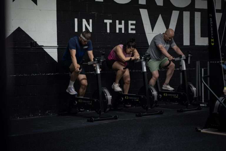 HYROX Doubles vs Singles: Which Should You Race First? Three athletes training side by side on BikeErgs during a HYROX class at Hunger in the Wild