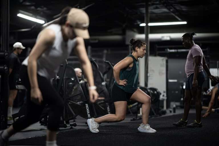 HYROX Weights by Division: Every Station, Every Category (KG & LBS) Coach checking an athlete's form on walking lunges during a HYROX training session