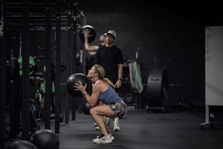 HYROX Pacing Strategy: Race Your First (or Fastest) Race Athlete squatting below parallel with a medicine ball during wall ball practice at Hunger in the Wild