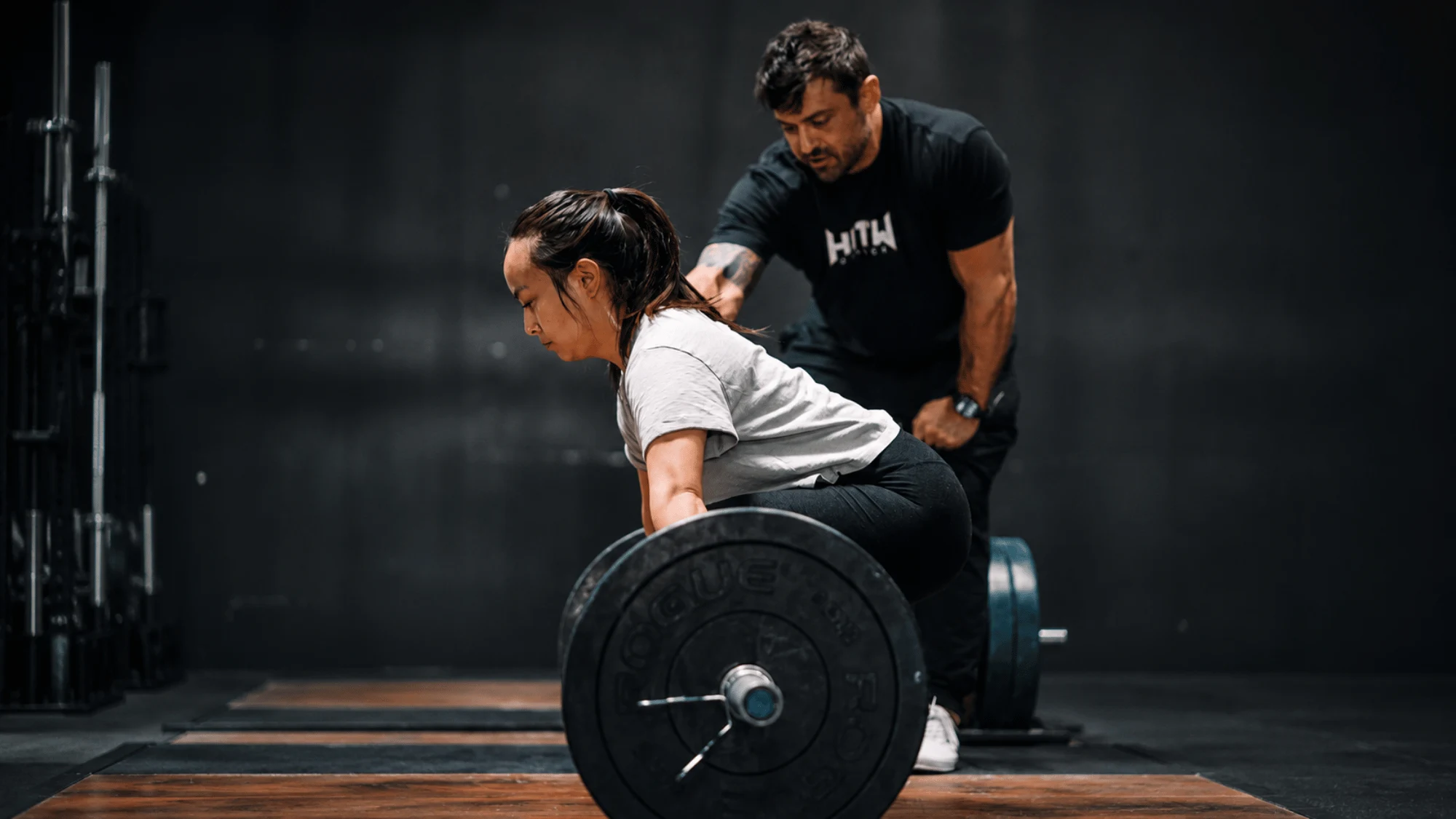 Fitness Coaching in Dallas What Real Coaching Actually Changes Coach provides hands-on guidance as an athlete sets up for a deadlift, reinforcing proper lifting technique during a personalized strength training session.