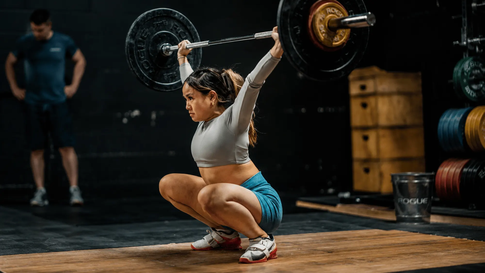 Woman performs an overhead squat with a loaded barbell, demonstrating strength, mobility, and Olympic weightlifting technique during training.