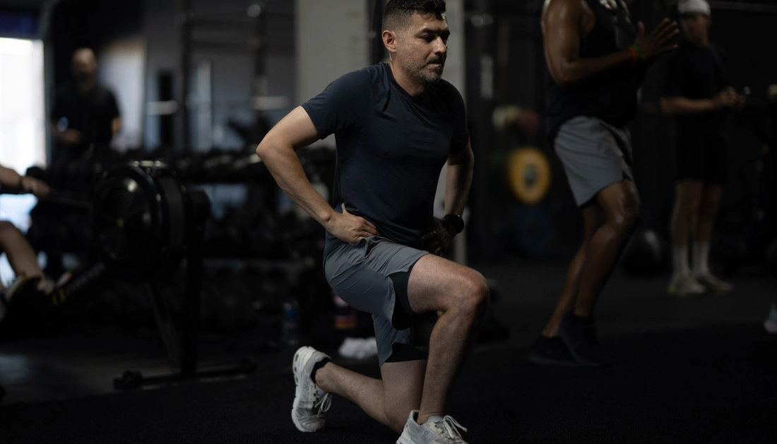 Muscle Building Gym in Dallas: What Actually Builds Muscle After 30 Man performing a bodyweight lunge alongside other athletes at Hunger in the Wild Gym.