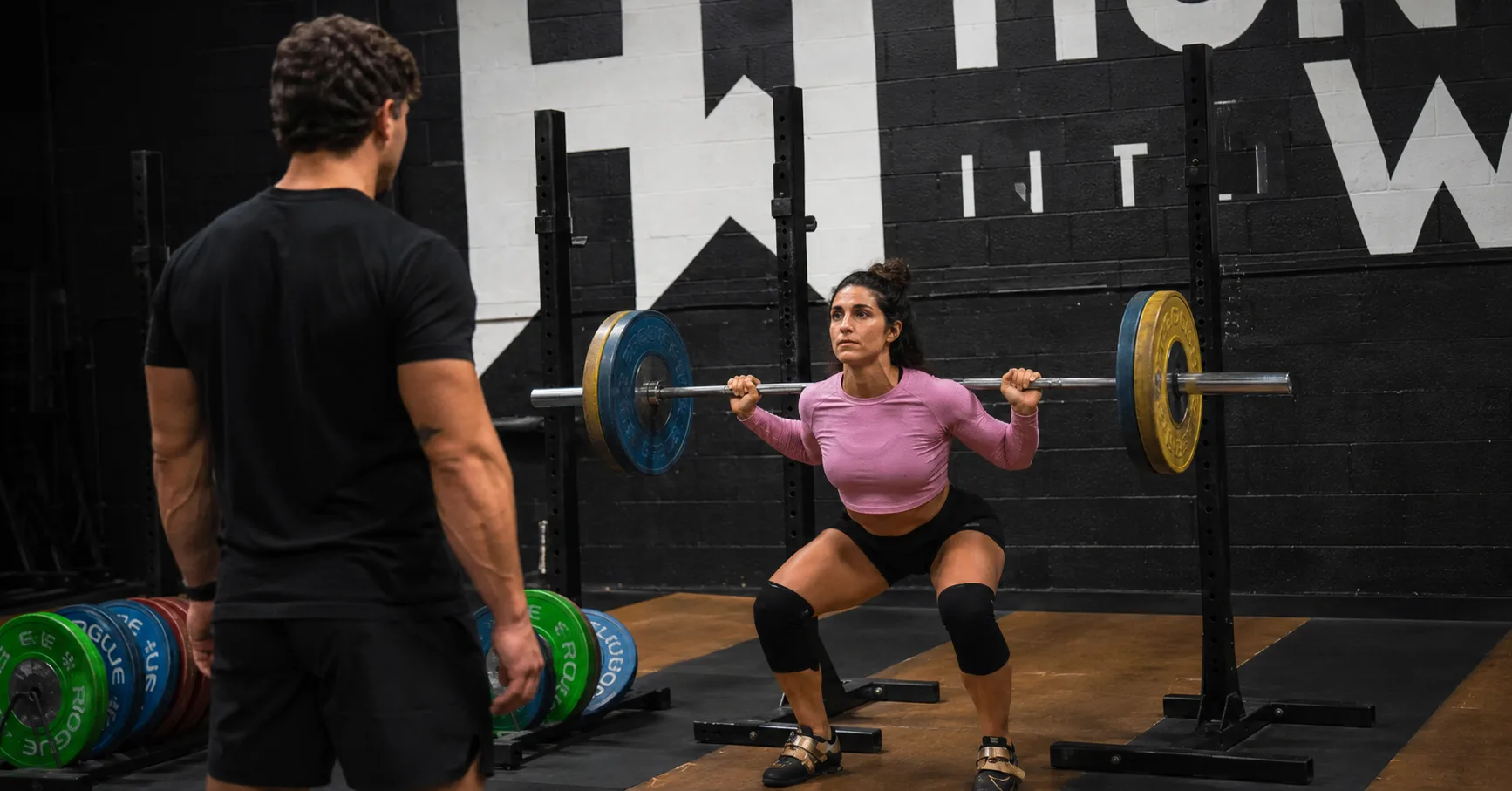 Best Weight Training Gym in Dallas for Serious Athletes Woman performing a barbell back squat with a coach at Hunger in the Wild Gym in Dallas.