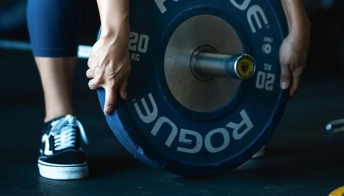 Starting Strength Training: What the First Six Months Actually Look Like A lifter loads a 20 kg plate onto the barbell at Hunger in the Wild Gym in Dallas.